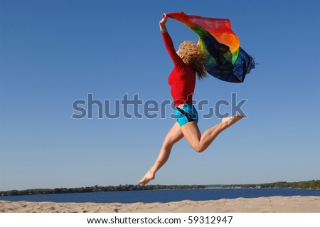 Athletic woman, wearing colourful clothes, jumps in the air with scarf in her hands.