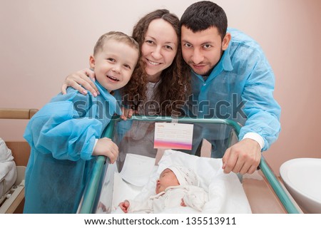 Happy family; father, mother, and son bending over their newborn daughter in the maternity hospital
