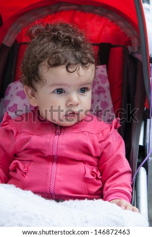 Portrait of baby girl sitting in stroller outdoors