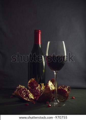 A bottle of good french wine, a piece of stemware and a pomegranate plus a couple of draperies.