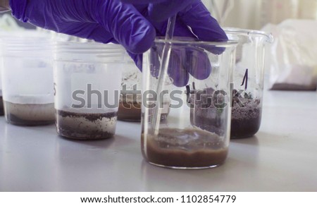 Close up hands of the scientist in laboratory mixing samples of the soil with water in the chemical beakers