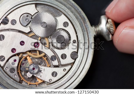 Close up of analog clock mechanics with finger winding it up