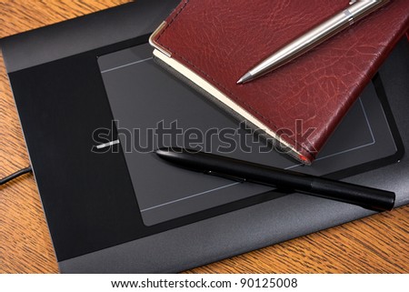 Graphic tablet on wooden table with digital pen, notebook and pencil