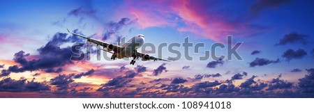 Jet plane is maneuvering for landing in a spectacular sunset sky. Panoramic composition.