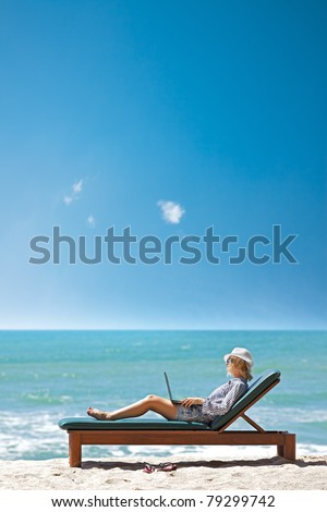 Young woman with laptop on a deck chair at the tropical beach. Vertical shot.