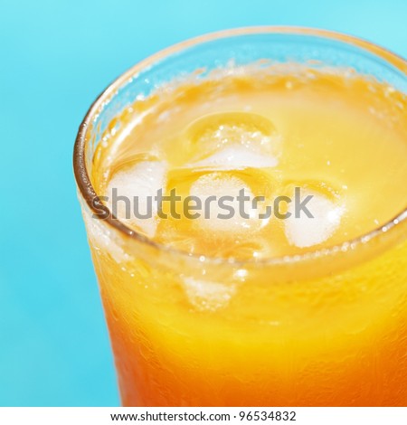 Closeup of a glass of orange juice with the ice against swimming pool. Shallow DOF. Square composition.