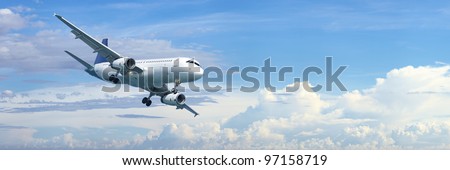 Jet plane in a blue cloudy sky is maneuvering for landing. Panoramic composition in high resolution.