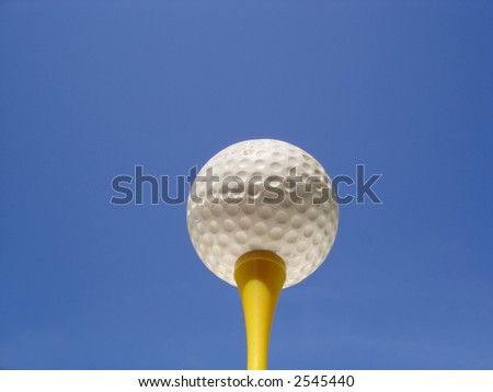Golf ball on tee against blue sky background
