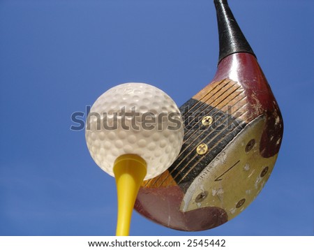 Golf ball on tee with club poised for drive against blue sky background