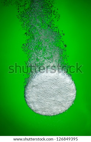 Effervescent tablet in water with bubbles on a green background