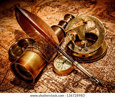 Vintage compass, goose quill pen, spyglass and a pocket watch lying on an old map.
