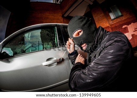 Robber and the car thief in a mask opens the door of the car and hijacks the car.