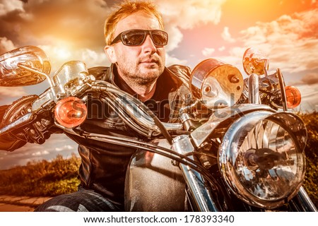 Biker man wearing a leather jacket and sunglasses sitting on his motorcycle looking at the sunset. Filter applied in post-production. Filter applied in post-production.
