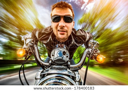 Biker man wearing a leather jacket and sunglasses sitting on his motorcycle looking at the sunset, racing on the road. Filter applied in post-production.