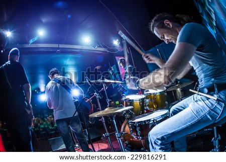 Drummer playing on drum set on stage. Warning - Focus on the drum, authentic shooting with high iso in challenging lighting conditions. A little bit grain and blurred motion effects.