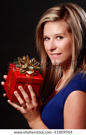 portrait of a beautiful young caucasian blond woman holding a wrapped gift isolated on black background