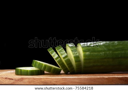 sliced english cucumber on wood plank, black background