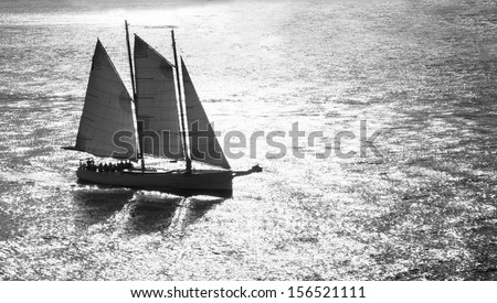 Black and white of sailboat sailing through suns reflection.