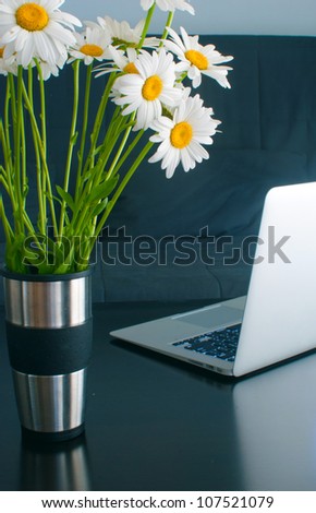 Laptop on the table and chamomiles in steel vase