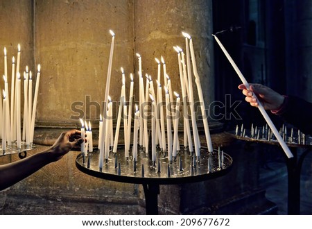 Hands of two persons offering a candle in catholic church in dark interior