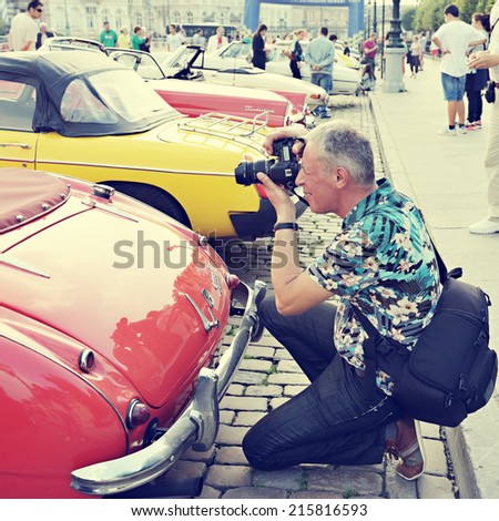BRUSSELS, BELGIUM-SEPTEMBER 07, 2014: Tourist takes a picture of a vintage car exposed during Comic Book Festival on Place des Palais. Vintage look filtering applied