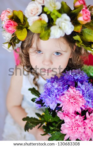 Little smiling girl with flower wreath and a bouquet of flowers