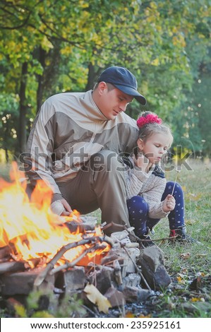 Little girl with her father roasting a marshmallow in the campfire