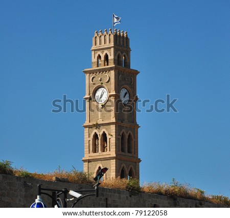 Clock tower in old Akko, with faces in Hebrew and Arabic, crowned with Israeli flag.