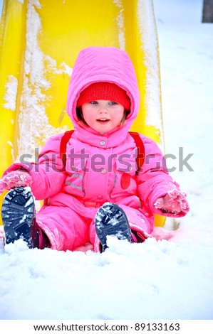 Adorable toddler girl sitting on the slide at winter day