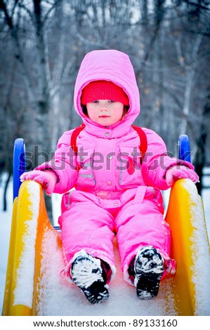 Adorable toddler girl sitting on the slide at winter day