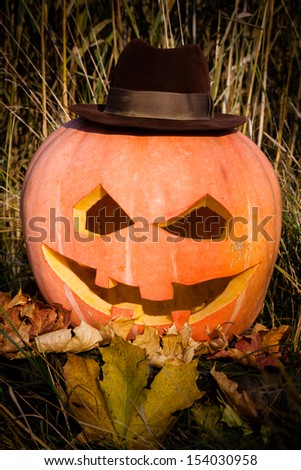 Halloween pumpkin face on autumn leave wear in hat