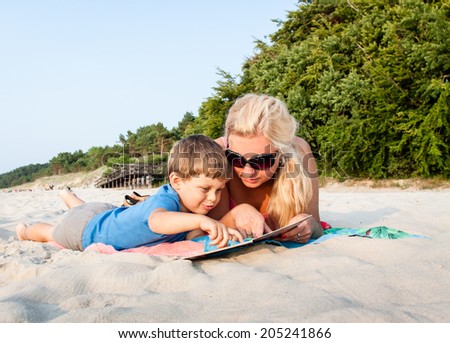 Mother and Mother and son sitting on sandy beach reading a book together