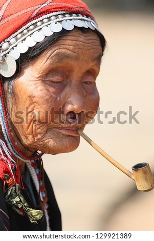 CHIANG RAI, THAILAND - FEB 26 : Akha hill tribe was smoking a pipe  with traditional clothes and silver jewelery in akha hill tribe minority village on February 26, 2013 in Chiang Rai, Thailand.