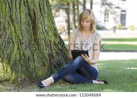 Young casual woman using digital tablet by tree on lawn