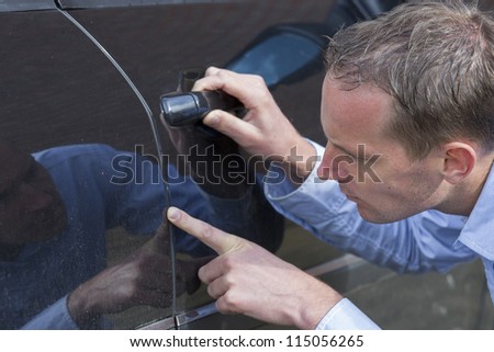 Mid adult man checking his car for scratches and dents. Horizontal shot.