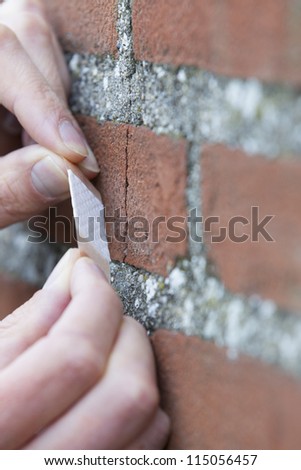 Man\'s hands applying duct tape over cracks in brick wall. Vertical shot.