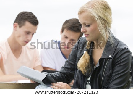 a young student is watching at her tablet. Two other students are learning at the background