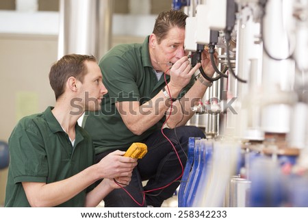 Senior technician and junior technician repairing agriculture machinery in a greenhouse