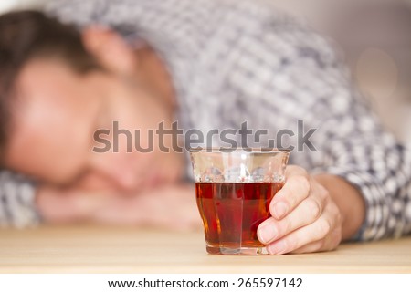 Young man feeling alone and drinking too much alcohol in his own home at the table