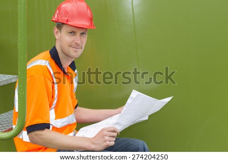 Side view portrait of confident architect holding blueprint while sitting in storage tank park