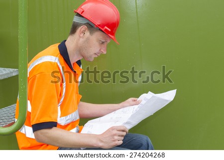Side view of male architect examining blueprint while sitting in storage tank park