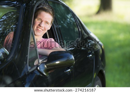 Portrait of happy young man driving car while looking out through window in park