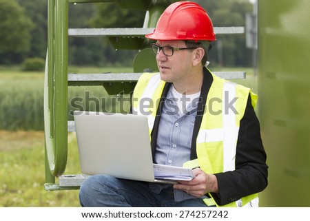 Mid adult architect holding blueprints while using laptop in storage tank park