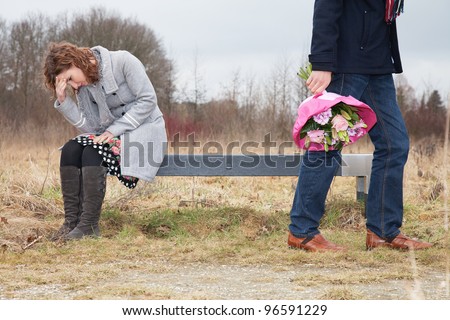 Man walking away with bouquet while woman sitting in sorrow on bench