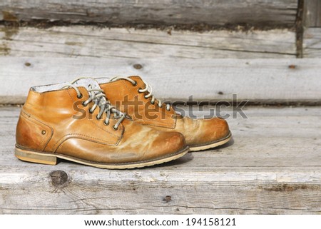 A pair of old leather boots on background wooden wall of a house