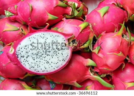 A Dragon Fruit sliced in half showing the white flesh and black seeds on a background of whole Dragon fruit. Image by Kevin Hellon.