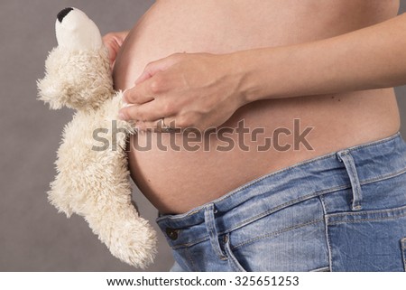 Mother holding a teddy bear on pregnant belly in third trimester.