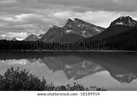 A lake in the Canadian Rockies shows its reflections of the mountains and sky; in black and white.