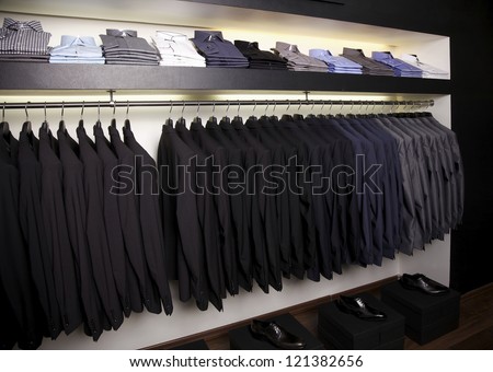 Suits on hangers and dress shirts in elegant clothing store.