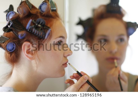 Attractive young woman applying make up in front of the mirror